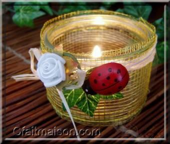 photophore avec un pot de laitage en verre bas et droit recouvert d'un ruban rustique, finition avec noeud en raphia naturel, lierre, coccinelle et fleurs.