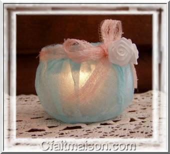 Photophore fait maison avec un pot de laitage en plastique recouvert d'une épaisseur de serviette bleue collée, finition avec un noeud rose et de fleurs blanches.