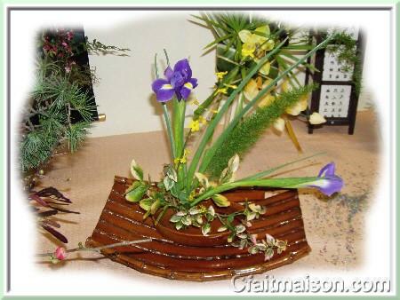 Composition dans un plat à four posé dans une corbeille asiatique en bambou avec pique-fleurs en fer, iris et fusain panaché.
