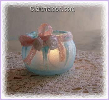 Photophore fait maison avec un pot de laitage en plastique recouvert d'une épaisseur de serviette bleue collée, finition avec un noeud rose et de fleurs blanches.